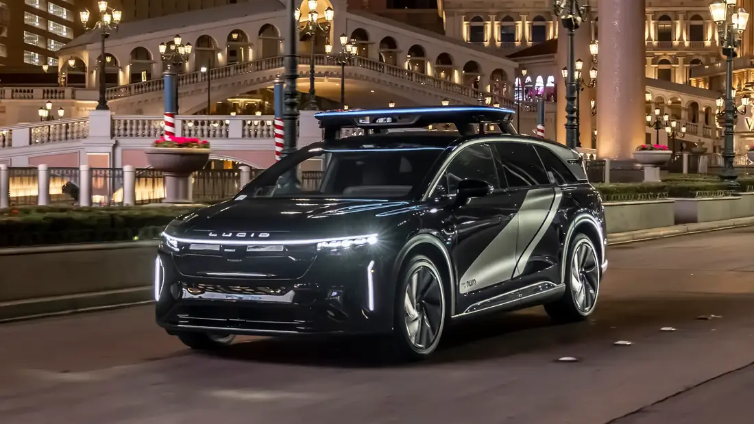 A black Lucid Gravity robotaxi with a lit sensor module on its roof, driving past the Venetian on the Las Vegas Strip at night